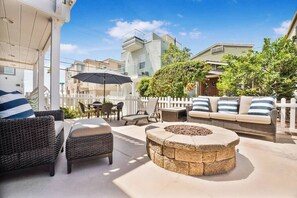 An outdoor patio area with wicker furniture, a stone fire pit, and a white picket fence.