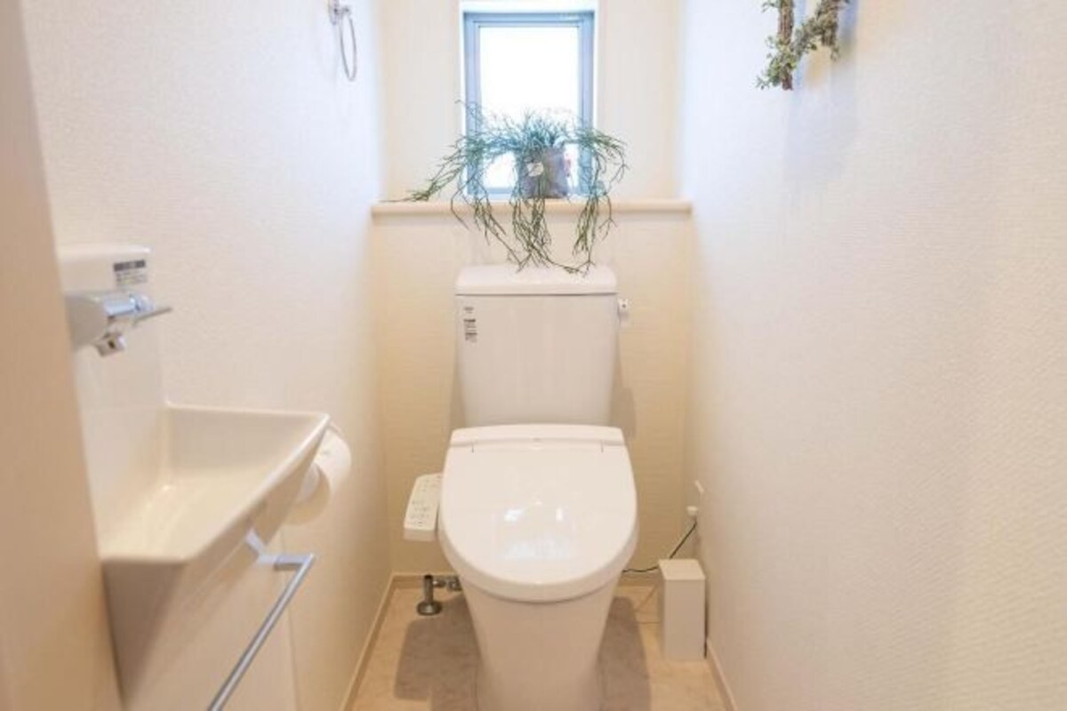 A small, narrow bathroom with a toilet, a sink, and a window above the toilet.