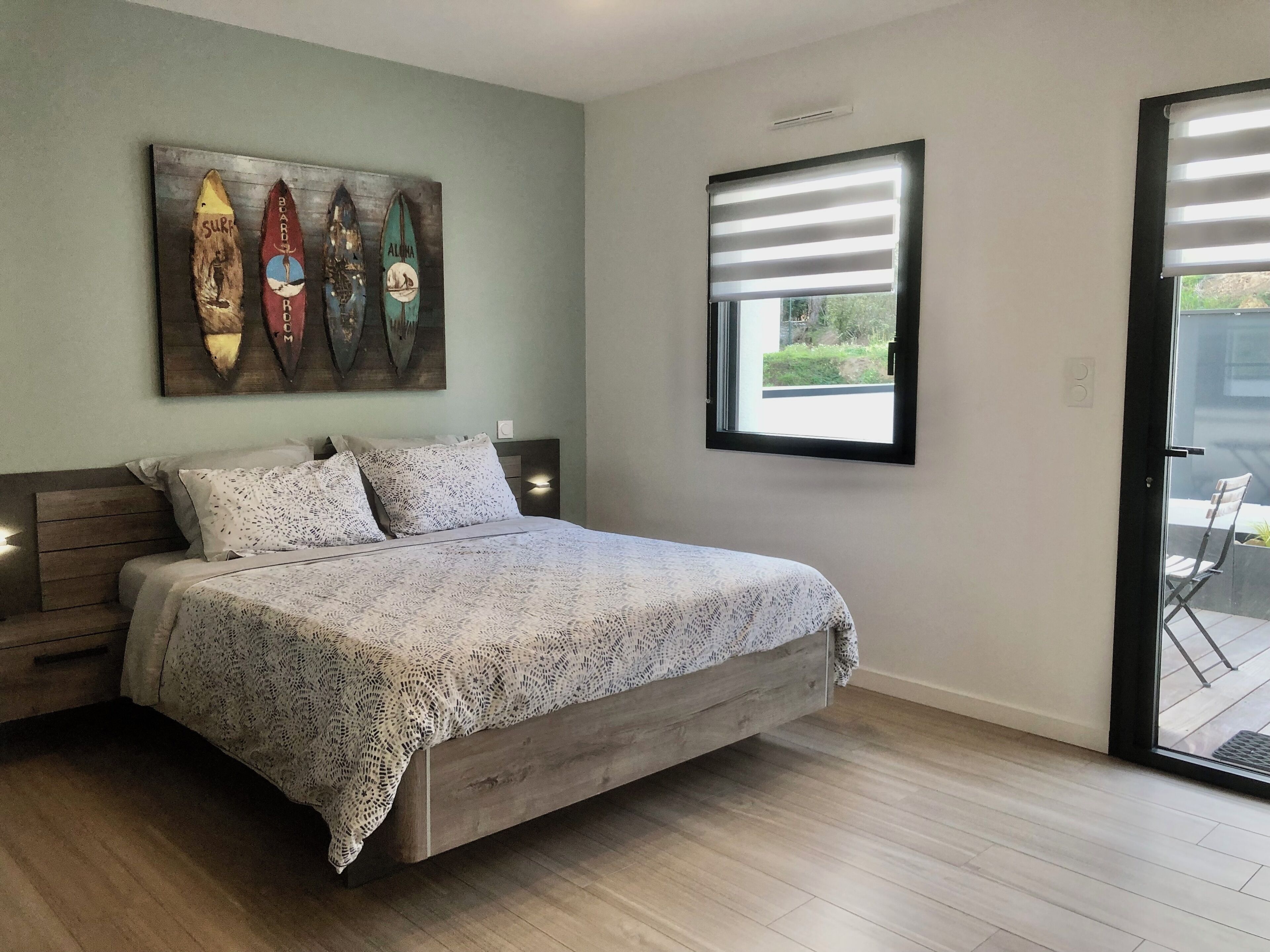 A bedroom with a wooden bed, a window with blinds, and a wall-mounted artwork of surfboards.