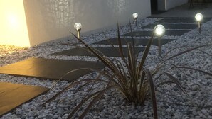 A garden area with a pathway, a plant with spherical lights, and a building in the background. - Quiet studio in the heart of Arradon (Arradon)