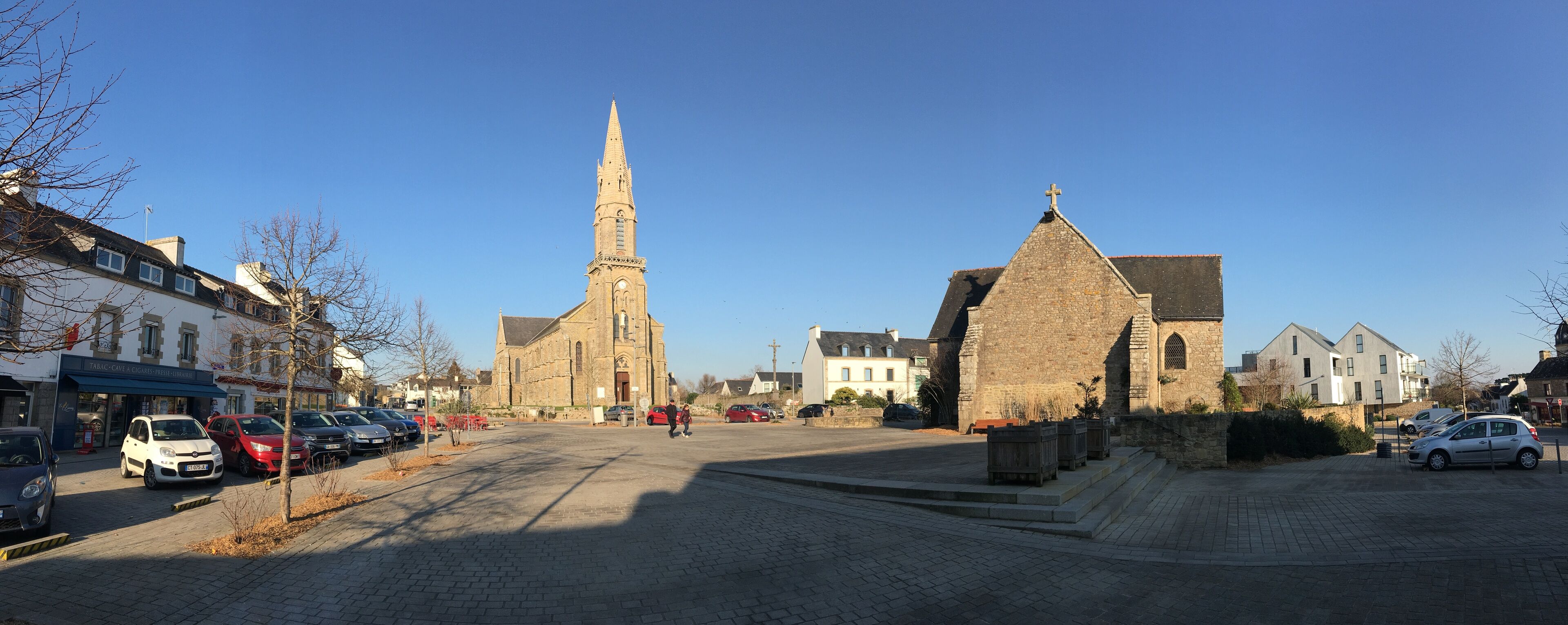 Eine Kopfsteinpflasterstraße mit historischen Gebäuden, darunter eine Kirche mit einem hohen Turm und ein kleineres Gebäude mit einem Kreuz auf dem Dach.