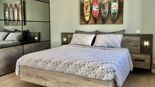 A modern bedroom with a large bed, a mirror, and a wall art piece of surfboards. - Quiet studio in the heart of Arradon (Arradon)
