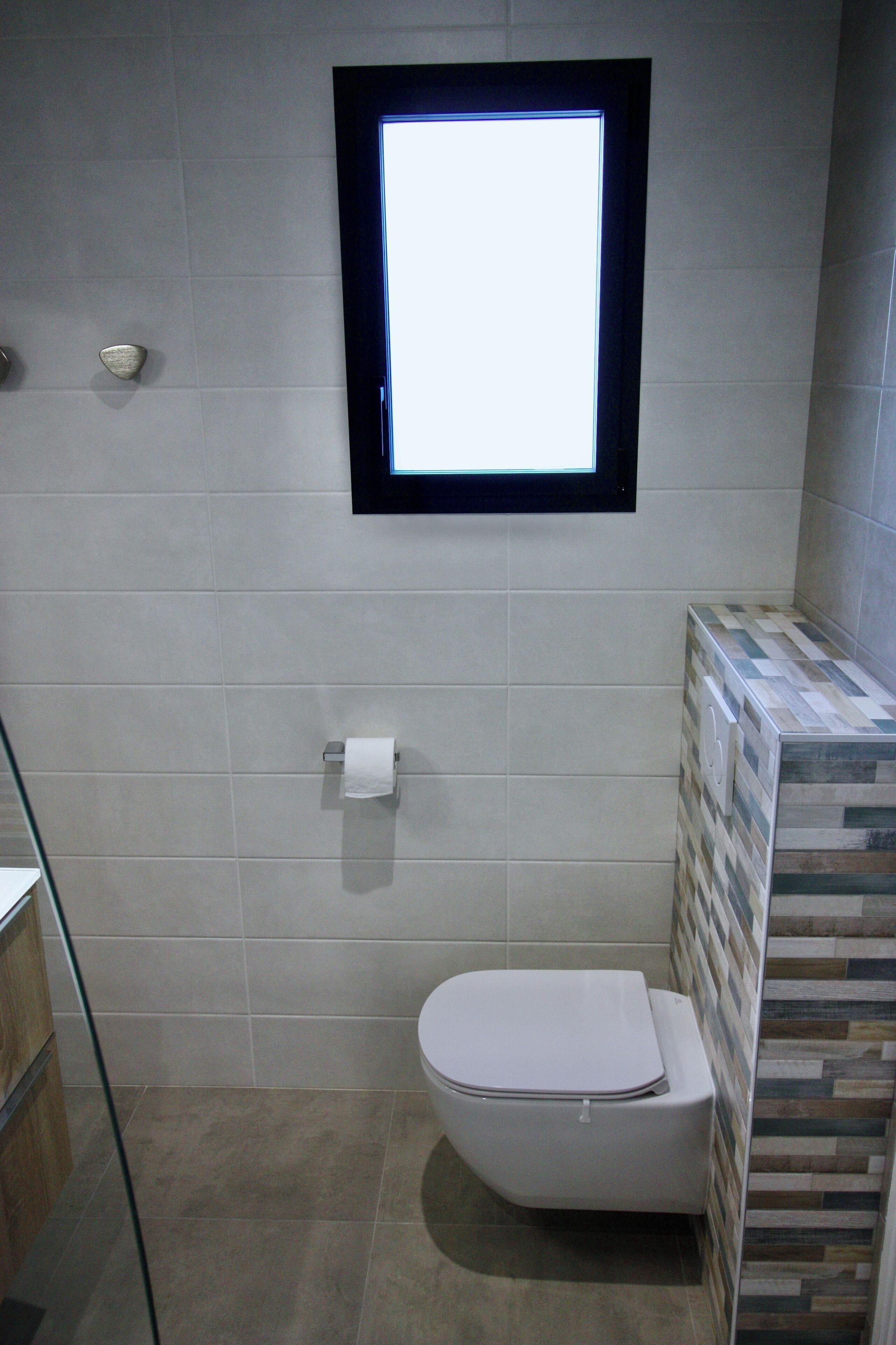 A bathroom with a toilet, a window, and a tiled wall.