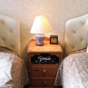 Un dormitorio con dos camas, una mesita de noche con lámpara, un reloj y un cajón.