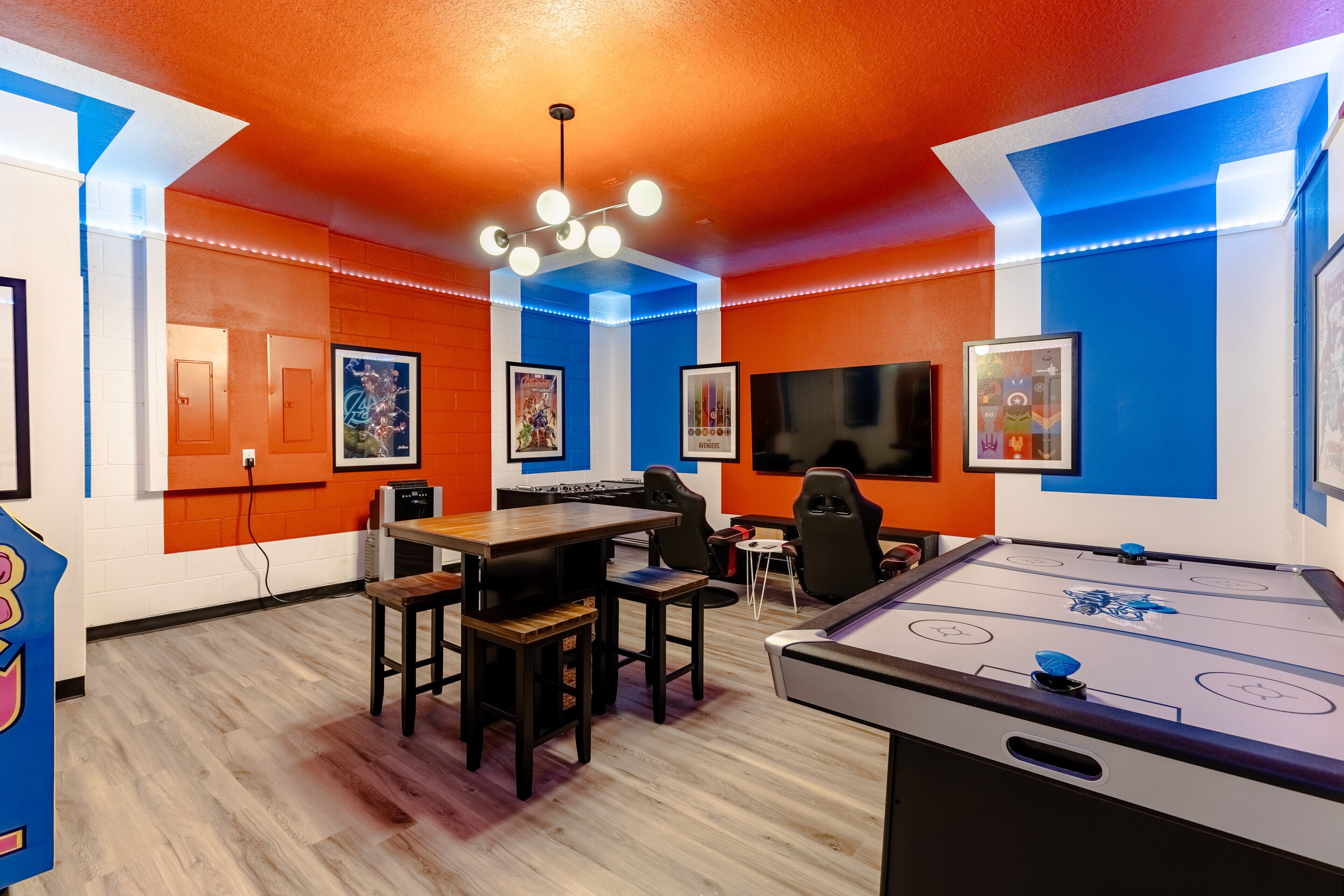 A room with a pool table, a foosball table, and a television. There are chairs and a table with a few people around it.