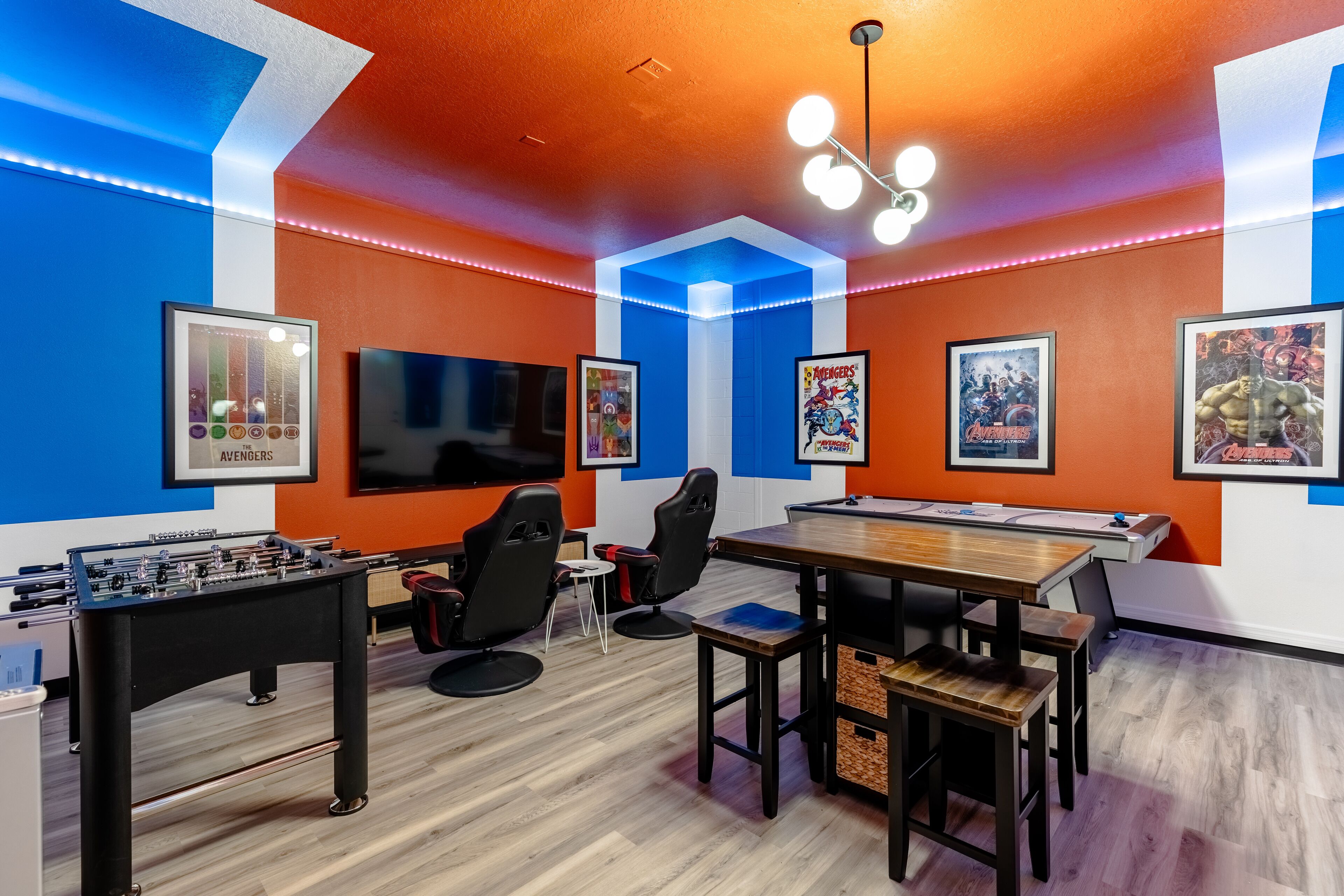 A room with a foosball table, gaming chairs, a wooden table, and posters on the walls.