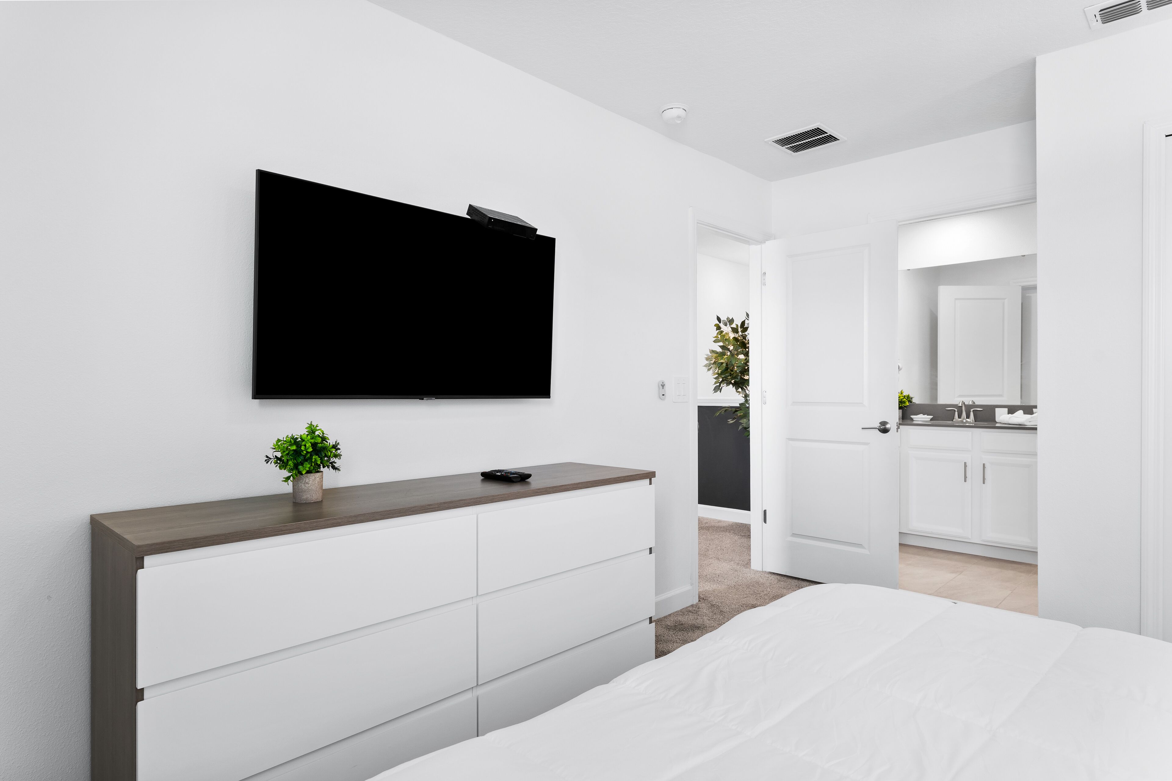 Een moderne slaapkamer met een groot bed, een dressoir, een flatscreen televisie aan de muur en een deur naar een badkamer en keuken.