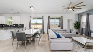 Un espace de vie moderne à aire ouverte comprenant un coin repas, un canapé et un ventilateur de plafond.