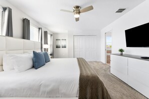 Un dormitorio moderno con una cama grande, ventilador de techo, televisor y vistas al exterior.