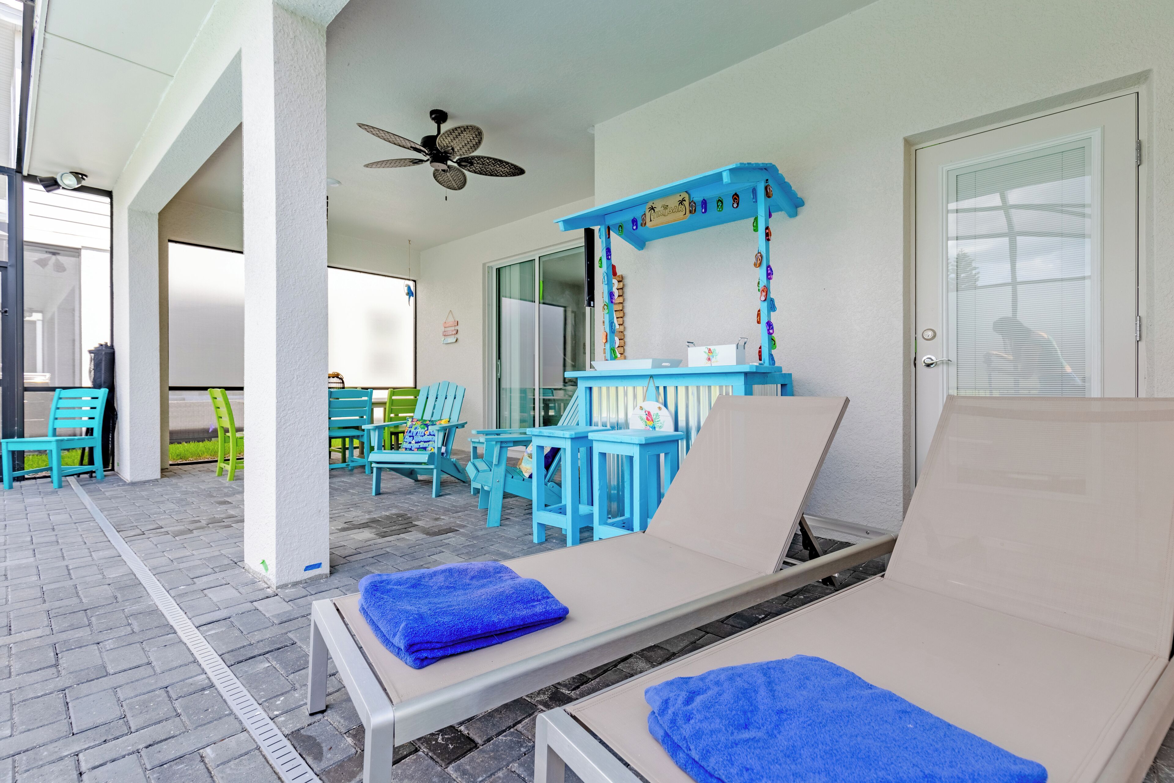 A covered outdoor lounge area with blue furniture, a ceiling fan, and a door leading to another room.