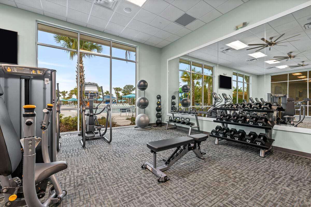 A gym with exercise equipment, mirrors, and large windows.