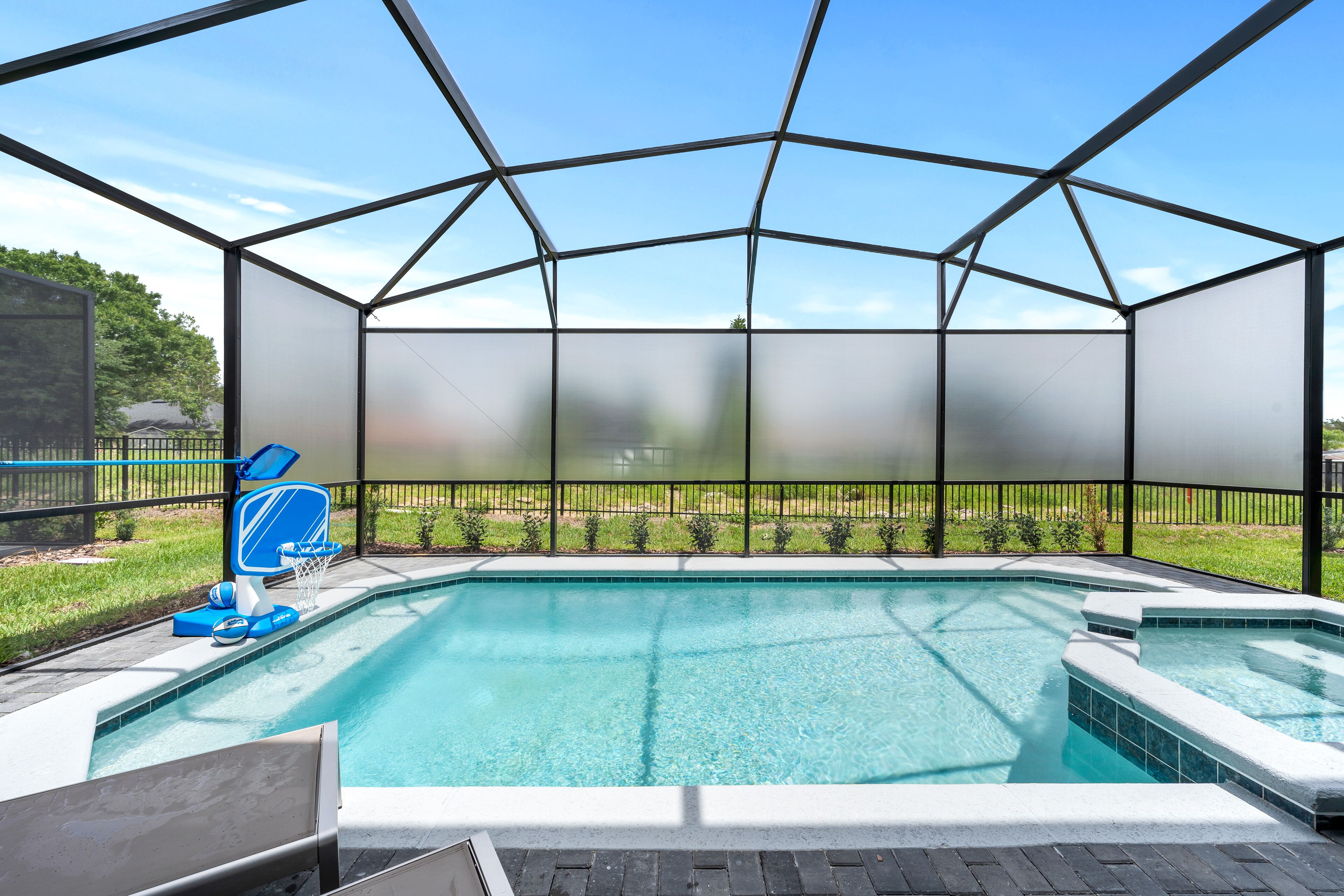Une piscine dotée d’une structure en verre, d’un panier de basketball et d’un jacuzzi.