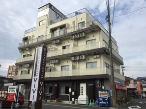 Un hôtel à plusieurs étages doté de balcons, une enseigne indiquant qu’il s’agit d’un hôtel d’affaires, et un distributeur automatique situé au rez-de-chaussée.
