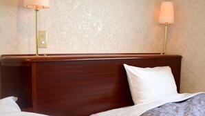 Habitación de hotel con dos camas, cada una con cubrecama estampado, cabecero de madera y dos lámparas de noche.