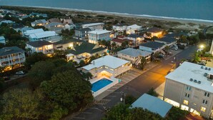 An aerial view of a coastal residential area with houses, a swimming pool, and a beach in the background. - Steps to the Beach | King Beds | Pool Access (Tybee Island)