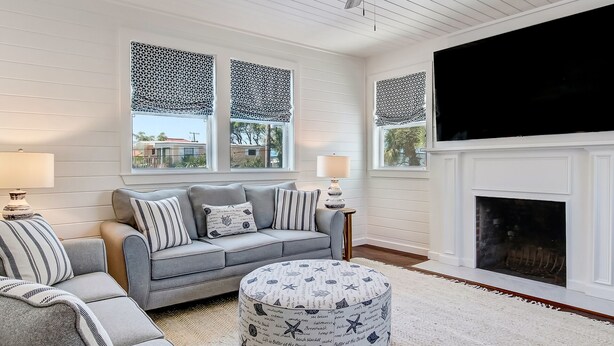 A living room with a gray sofa, ottoman, and patterned cushions, a fireplace, and a ceiling fan. - Steps to the Beach | King Beds | Pool Access (Tybee Island)