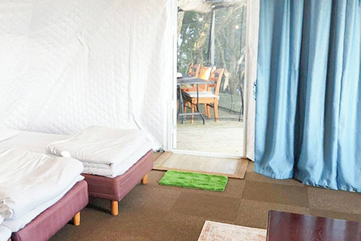 A room with two beds, a wooden floor, a green rug, and a view of an outdoor area with a table and chairs.