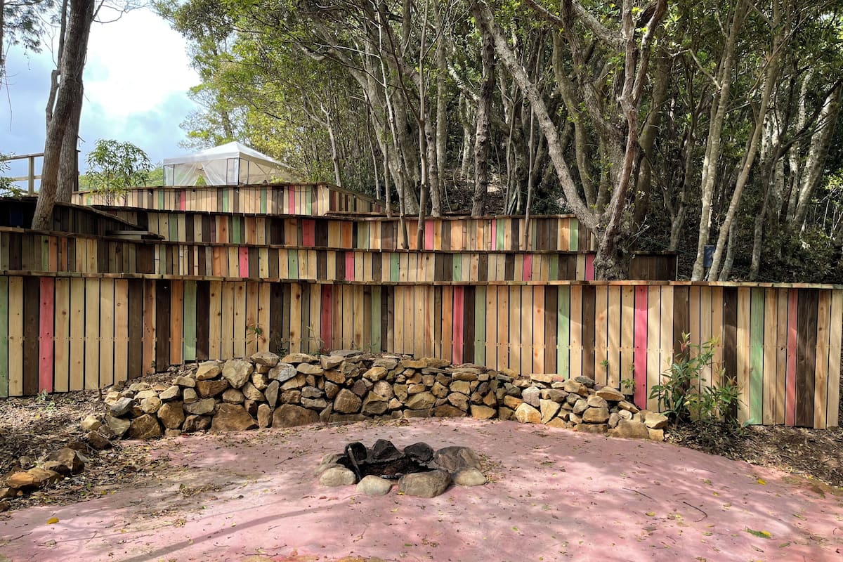 A wooden fence with colorful vertical stripes, a stone wall, and a pink surface area.