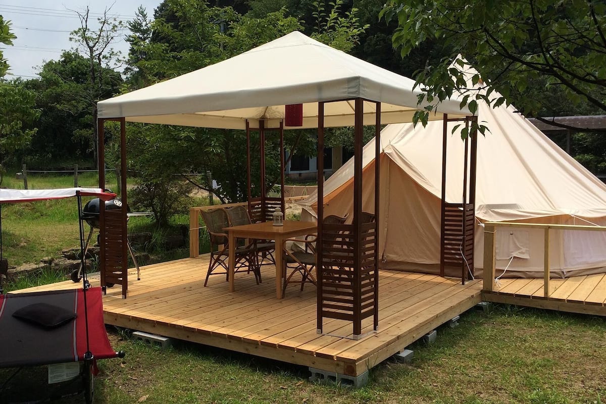 A tented outdoor area with a table and chairs, a grill, and a covered seating area.