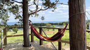 A hammock on a wooden deck overlooking a landscape with trees and a view of the ocean. - Yamamizuki (Shimanto)