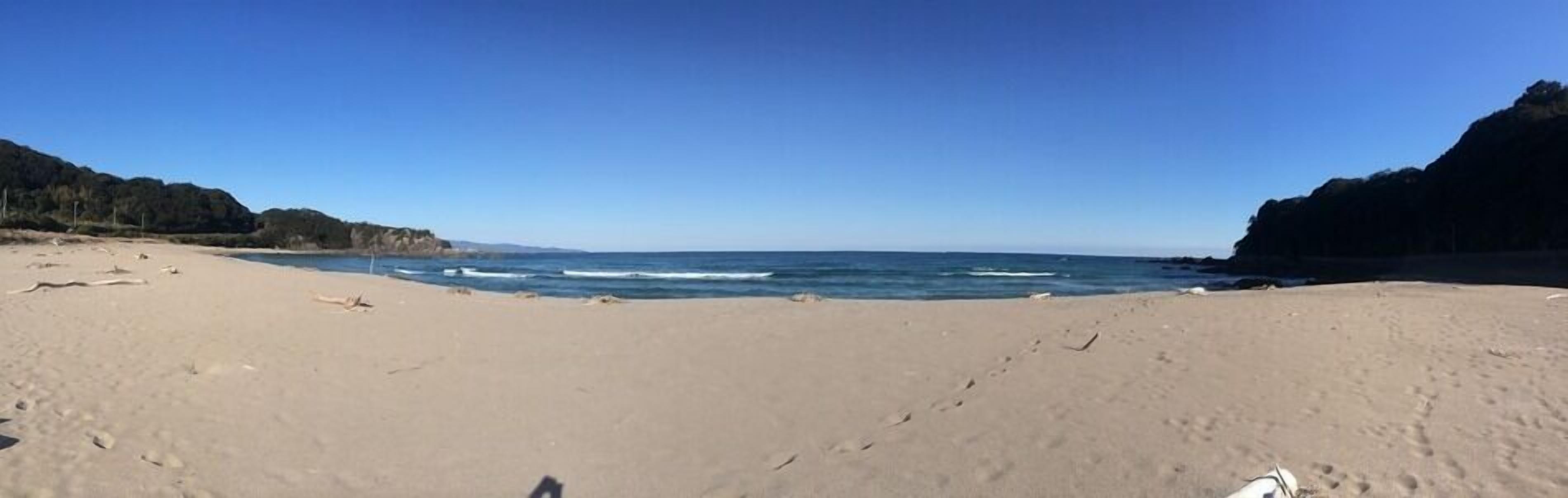 A beach with a clear sky, sandy shore, and rocky cliffs.