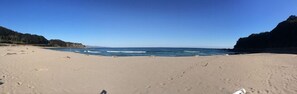 A beach with a clear sky, sandy shore, and rocky cliffs.