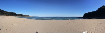 Una playa con cielo despejado, orilla arenosa y acantilados rocosos.