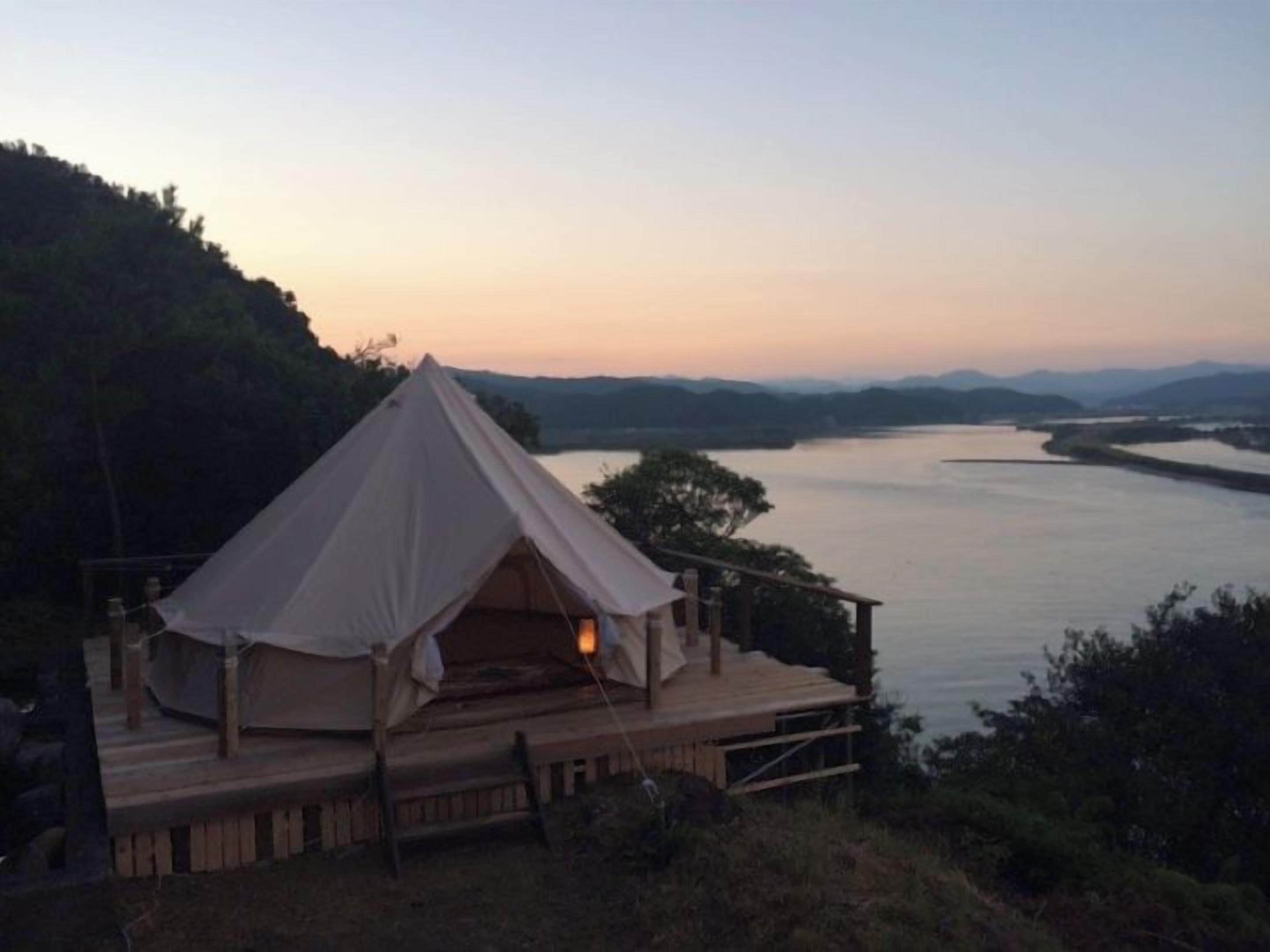 A tented accommodation with a wooden deck, overlooking a calm body of water and distant mountains.
