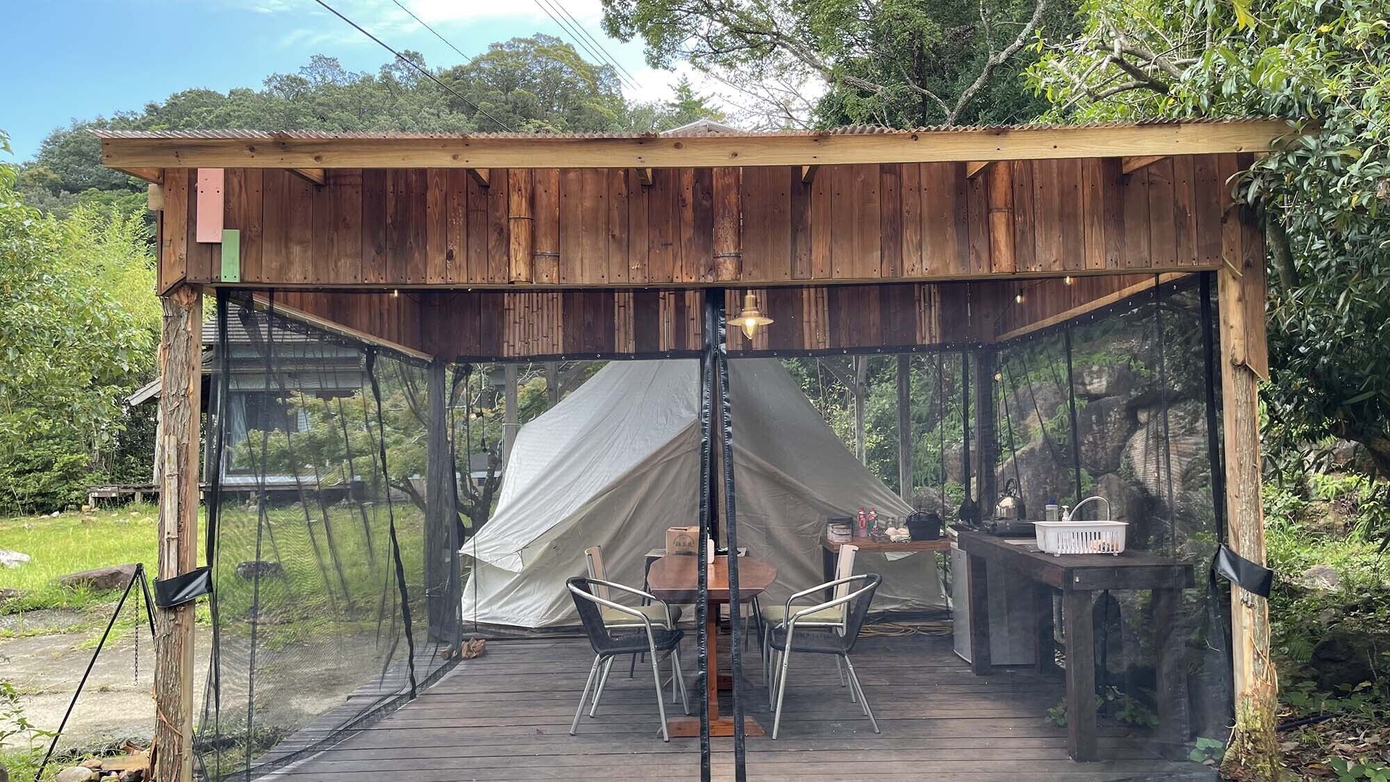 Eine Holzhütte mit Zelt, Tisch, Stühlen und Spüle.