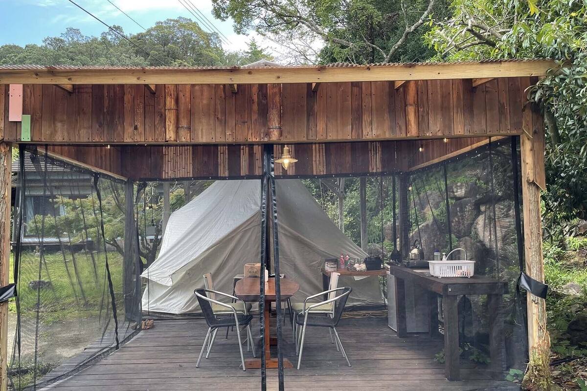 A wooden structure with a tent, a table, chairs, and a sink.