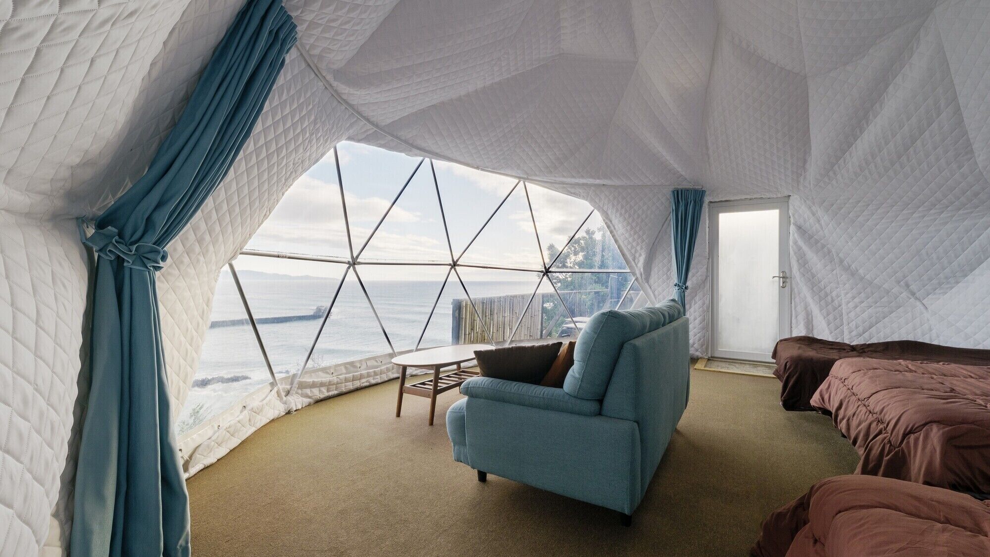 Ein Zelttraumzimmer mit Blick auf den Ozean, einer Couch, einem kleinen Tisch und einem Bett.