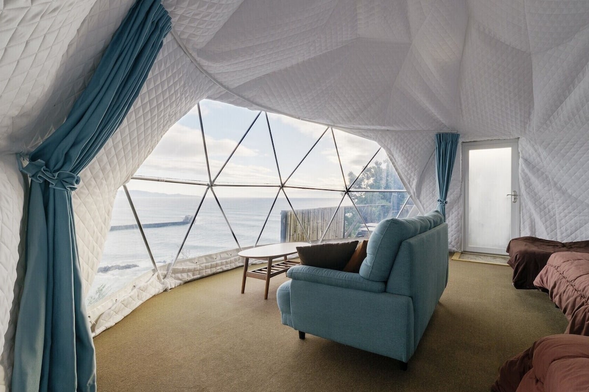 A tent-style room with a view of the ocean, a sofa, a small table, and a bed.