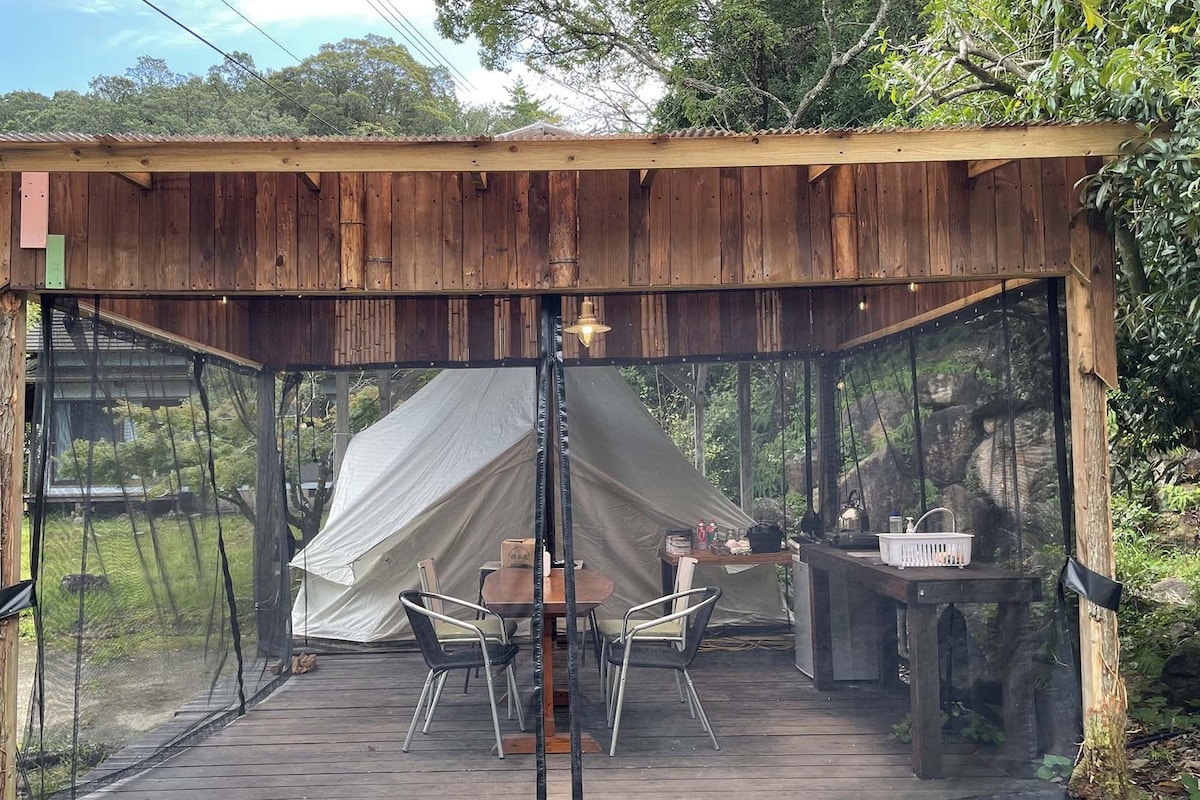 A wooden structure with a tent, a table, chairs, and a sink.