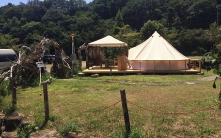 A tented accommodation with a flat roof, surrounded by a grassy area and a forested hill.