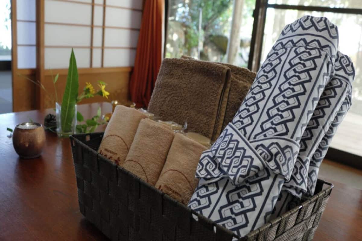 A woven basket with towels and a patterned cloth on a wooden table.