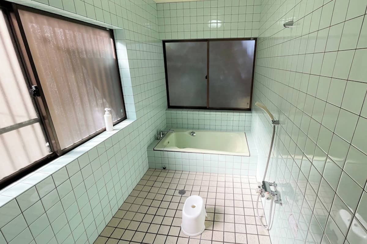 A small bathroom with a bathtub, a window with a blind, and a toilet.