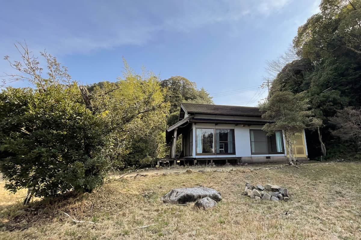 A small house with a porch, surrounded by trees and rocks.