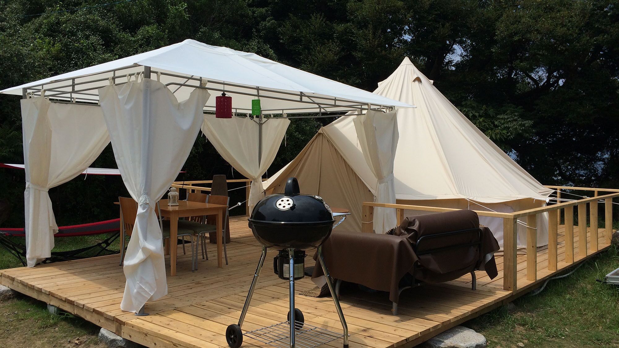 Ein Zelten-Bereich im Freien mit Grill, Sitzgelegenheiten und einer Terrasse.