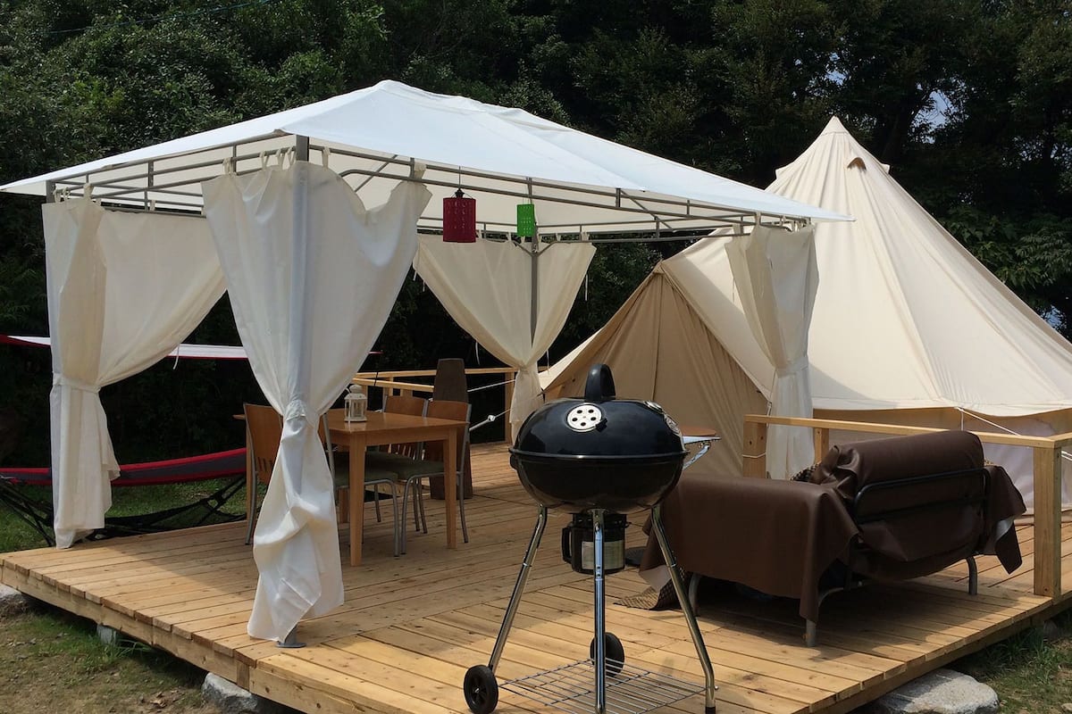 A tented outdoor area with a grill, seating, and a deck.