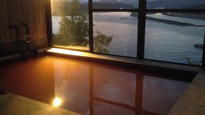 A room with a large window overlooking a body of water, a wooden floor, and a bench.