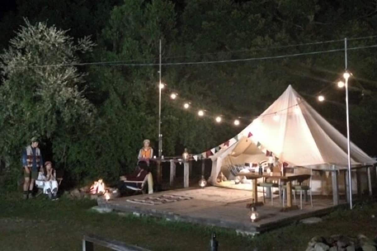 A tented outdoor area with string lights, a fire pit, and a table set up for dining.