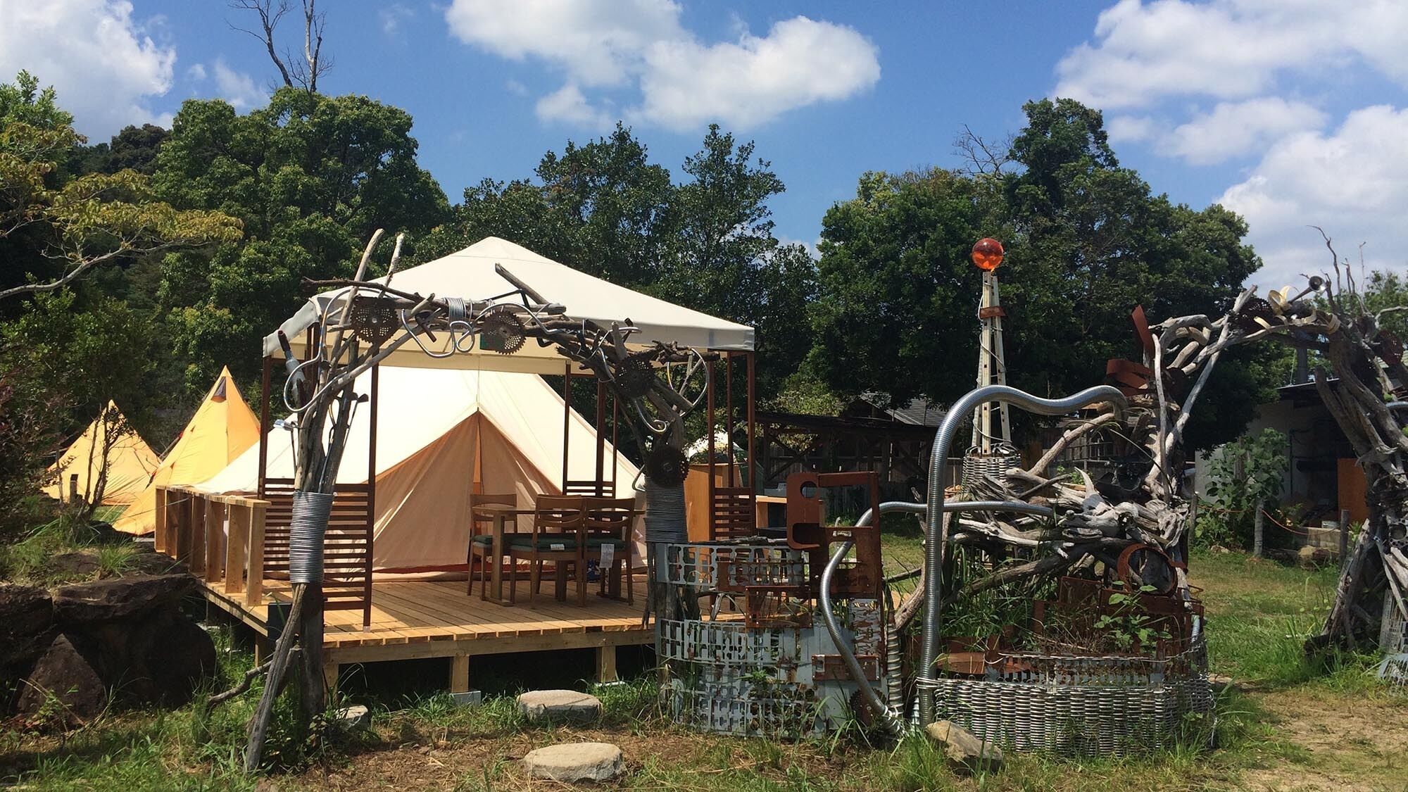 Eine Zelthütte mit Holzterrasse, Sitzgelegenheiten und einer dekorativen Metallkonstruktion.