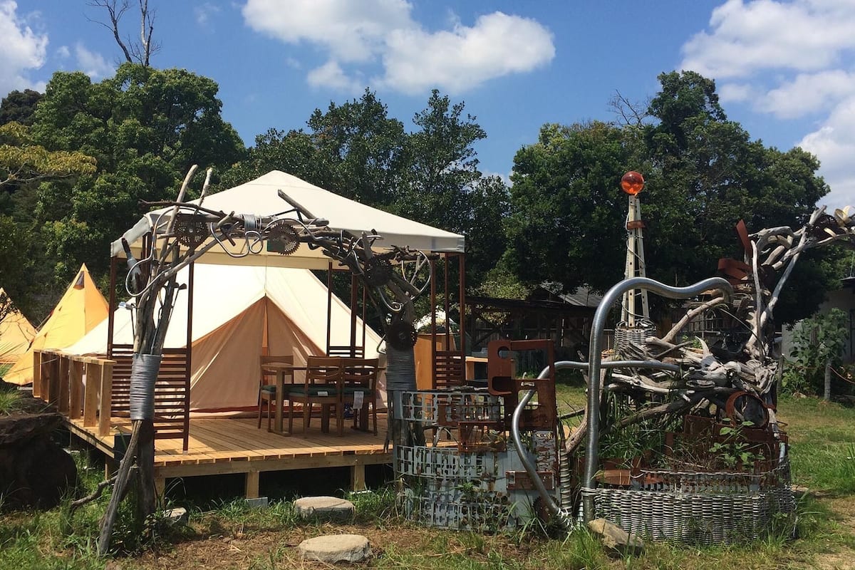 A tented accommodation with a wooden deck, seating, and a decorative metal structure.