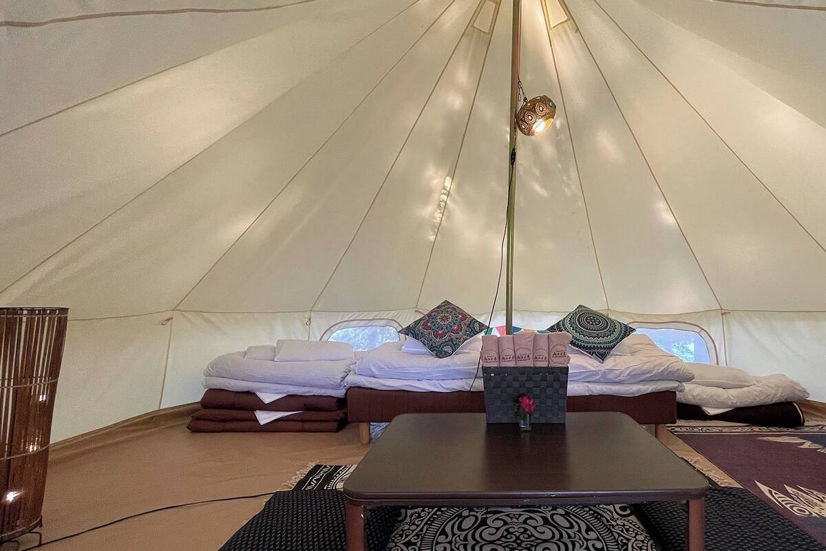 A tent with a bed, pillows, a table, and a small vase with a flower.