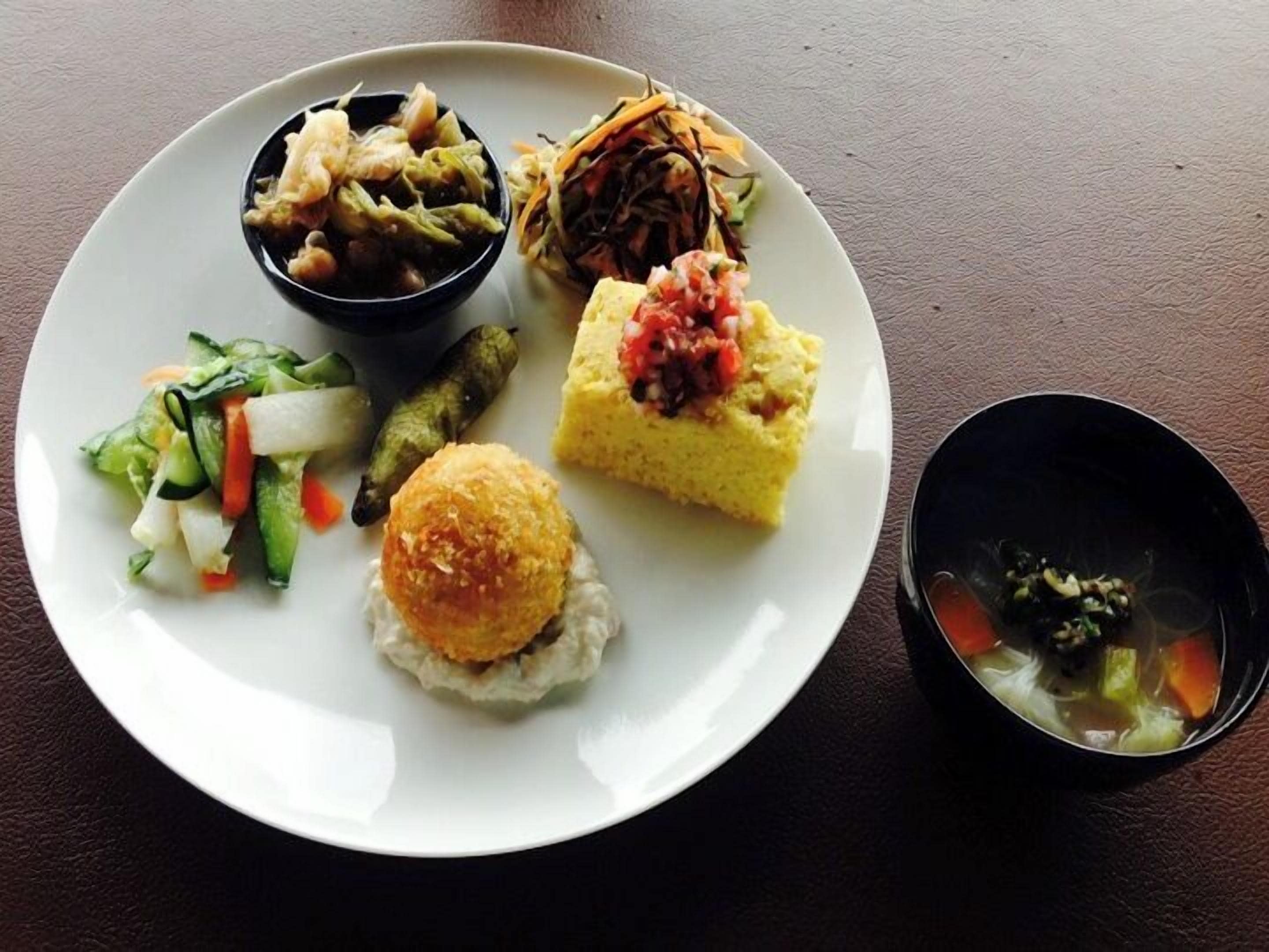 A plate with various food items including a salad, a bread roll, a small bowl of soup, and a piece of cake.