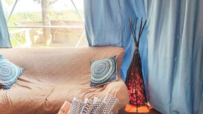 A beige sofa with patterned cushions, a decorative vase, and a window with blue curtains. - Yamamizuki (Shimanto)