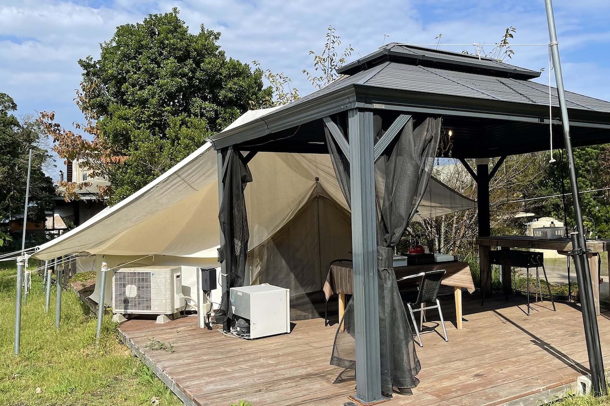 A covered outdoor area with a table and chairs, a grill, and a tent.