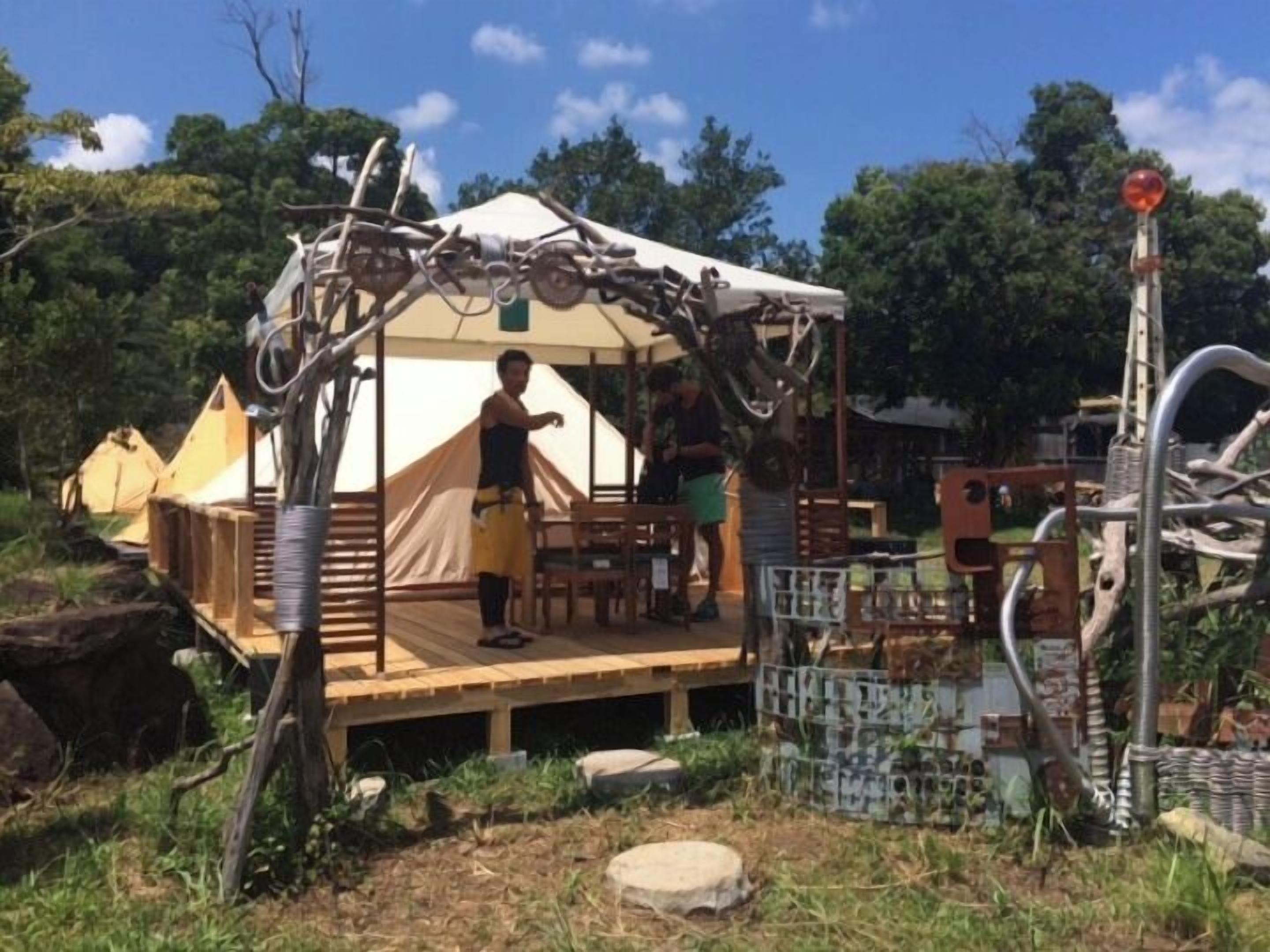 A tent with a wooden deck, surrounded by trees and a metal fence.