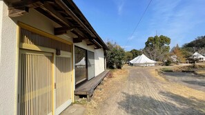 A building with a wooden deck, a covered outdoor area, and a dirt path leading to a white tent.