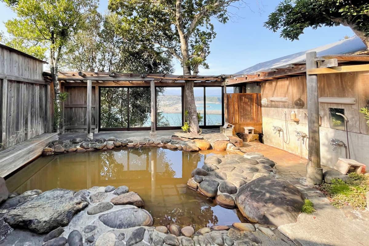 A rustic outdoor area with a stone pond, wooden deck, and a view of a natural landscape.